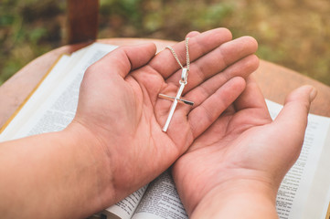 Woman holding a the cross in hand against the background of the bible. 
