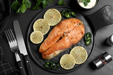 Delicious roasted fish served on black table, flat lay