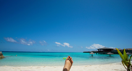 Fototapeta na wymiar Feet tourist relax at Maldives turquoise sea white sand tropical beach paeadise