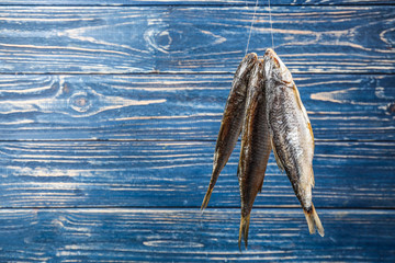 Dried fish hanging on rope against blue wooden background. Space for text