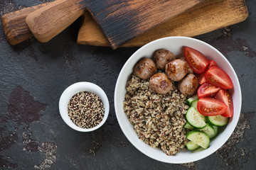 Top view of quinoa, roasted meatballs and fresh vegetables served in a bowl over brown stone background, horizontal shot