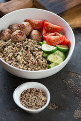 White bowl with fried meatballs, quinoa and vegetables, vertical shot on a brown stone surface, close-up