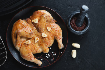 Black plate with pan fried chicken tapaka, flatlay over black stone background, horizontal shot