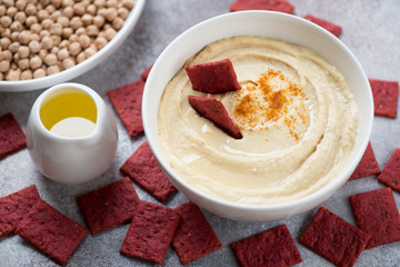 Hummus served in a white bowl with olive oil, paprika and beetroot crackers, studio shot