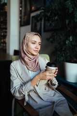 muslim woman with a thoughtful look sits in a cafe and holds coffee in her hand