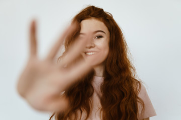 red-haired brown-eyed beautiful girl with a smile makes a prohibitory gesture with his hand, pushing away the camera