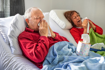 Elderly couple lying on the bed and blow their nose