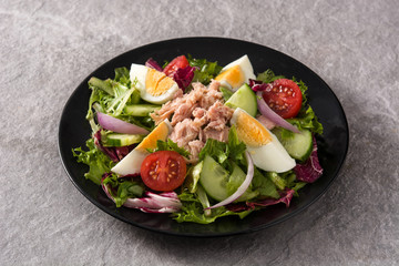Salad with tuna, egg and vegetables on black plate and gray background