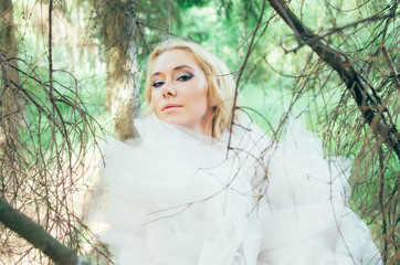 Naklejka premium Portrait of young blond bride in forest through branches