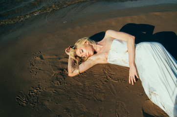 Portrait of young blond bride lies on sand among the water