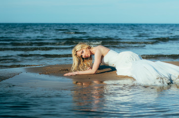 Portrait of young blond bride lies on sand among the water