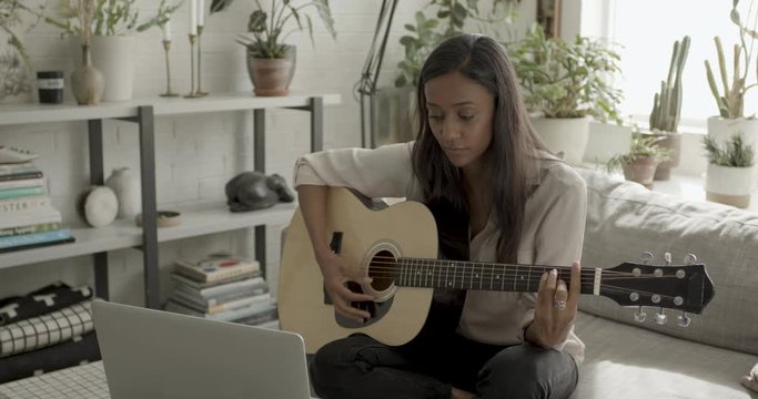 Woman learning to play guitar at home with laptop