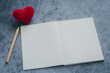 Pencil and plain notebook with red heart symbol black background with copy space. Concept of quotes...
