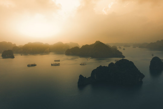 Aerial image of Ha Long Bay during sunrise in Autumn 2019 with cruise ships and junk boats anchored in the bays