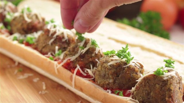 hand sprinkle fresh parsley on meatball sandwich close up