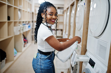 Cheerful african american woman hold detergent near washing machine in the self-service laundry.