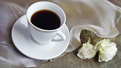 A Cup of fragrant coffee and white roses on a transparent napkin.