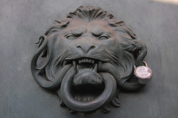 door hammer in shape of lion head with a snake in its mouth and a lock in its ear on massive gates in Paris, France