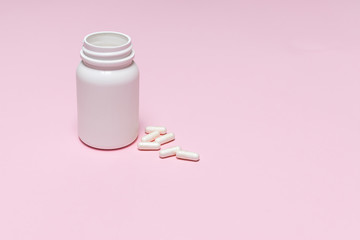 White medical capsules in white plastic bottle on light pink background with copy space for your...
