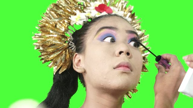 Balinese dancer applying mascara on her eyelashes in the studio. Shot in 4k resolution with green screen background