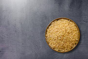 Parboiled brown rice in ceramic bowl at dark slate background. Close up shot. Top view.