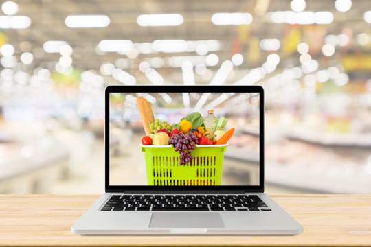 supermarket aisle blurred background with laptop computer and shopping basket on wood table grocery online concept