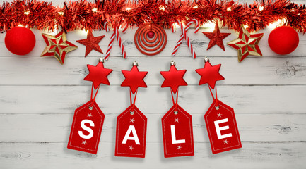 Golden star christmas lights, and christmas baubles, on a destressed white wooden background, above hanging tags spelling sale