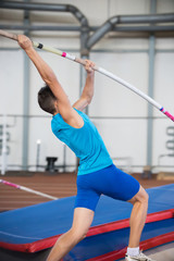 Fototapeta na wymiar Pole vaulting indoors - young man leaning on the pole and about to jump