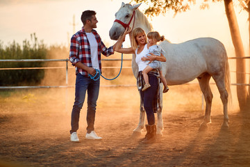 Smiling family with girl in a horse farm petting horses