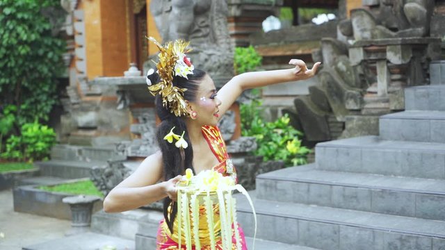 Slow motion of attractive balinese dancer holding a frangipani flower while dancing in the temple