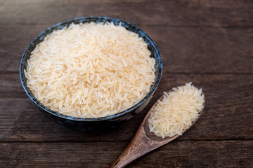 Parboiled Rice ligth colour in a ceramic bowl and wooden spoon placed on a wooden table in natural light. Close up shot. 45 degree angle.
