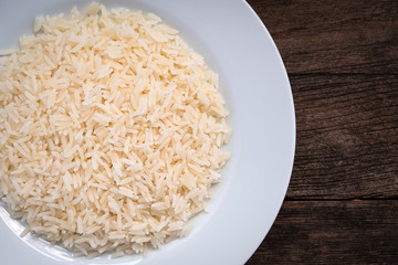 Parboiled cooked rice in a white ceramic plate. Parboiled rice on a wooden table. Parboiled rice Products exported from Thailand. Parboiled rice ligth colour. Parboiled rice close up shot. top view.