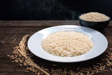Parboiled Rice uncook in dark ceramic color and paboiled rice cooked in a white ceramic plate placed on a wooden table. Parboiled rice close up shot. Parboiled rice top view.