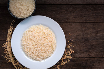 Parboiled Rice uncook in dark ceramic color and paboiled rice cooked in a white ceramic plate placed on a wooden table. Parboiled rice close up shot. Parboiled rice top view.