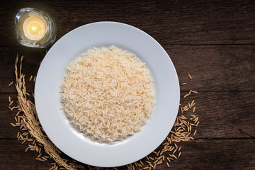 Parboiled Rice cooked rice in a white ceramic plate placed on a wooden table and candle.