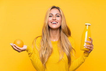 Young blonde woman holding an orange juice over yellow background