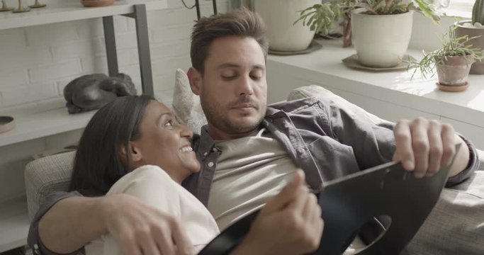 Young adult couple looking at music record at home on sofa