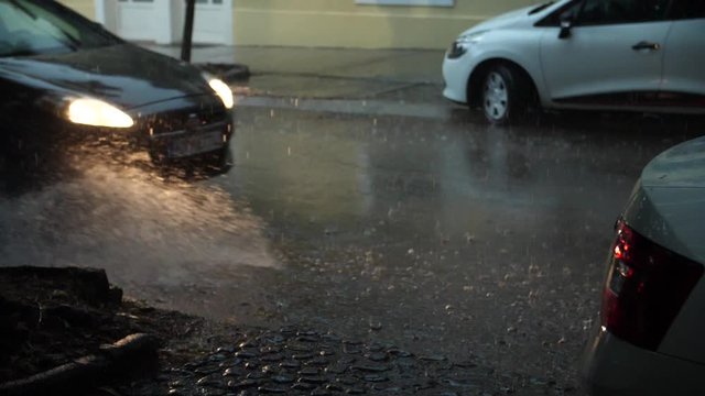 Slow motion shot of cars passing through a flooded street in heavy rain