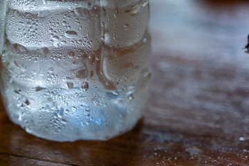 Clear water drop on cool water bottle on wooden table with blur background