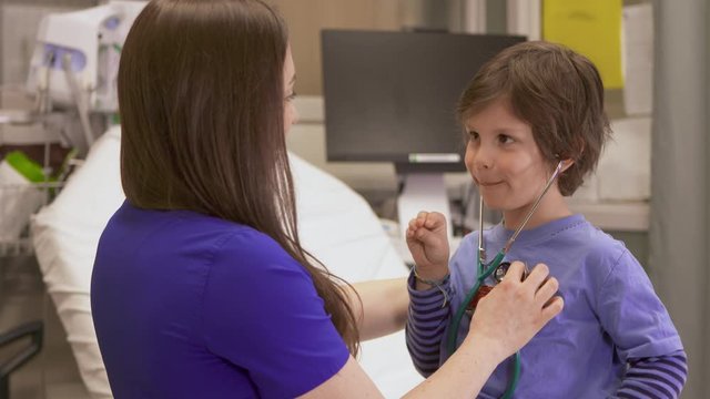 A nurse let's a little boy hear his own heartbeat and he is happy and surprised.