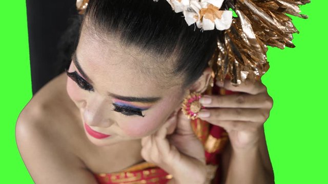 Balinese dancer wearing earrings accessories on her ear in the studio. Shot in 4k resolution with green screen background