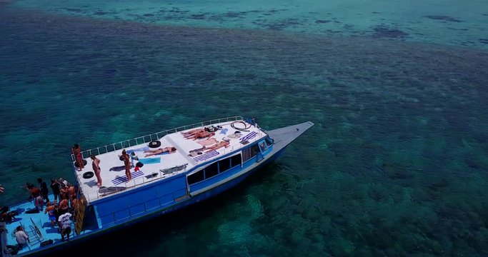 Men And Women Having Fun Riding On A Cruise Ship, Jumping Into The Water, Sunbathing, Snorkeling With Many Coral Reefs Underwater In Caribbean - Aerial Shot
