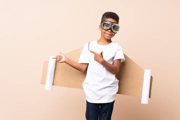 African American boy  with aviator hat and with wings and pointing to the lateral over isolated background © luismolinero