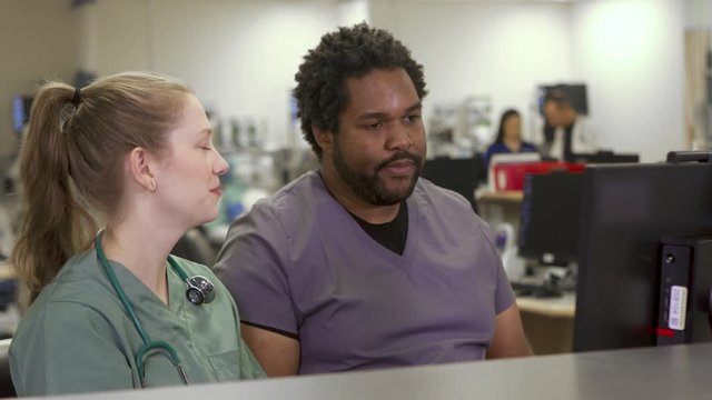 Diverse medical team at a computer in a hospital. Caucasian blonde female nurse and a black male nurse sitting at the nurses station.
