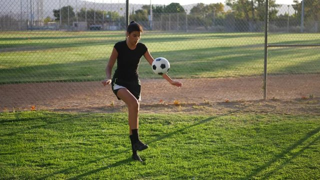 A female college athlete soccer player juggling a football in slow motion during soccer team practice.