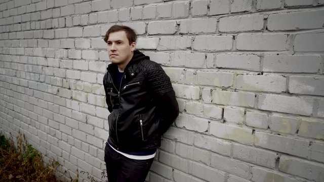 Man in a black leather jacket. Sad male looking to the side. Young man in a black leather jacket at the background of a brick wall