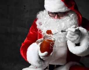 Portrait of Santa Claus holding spoonful and a jar of red caviar fish salmon on dark gray. New year...