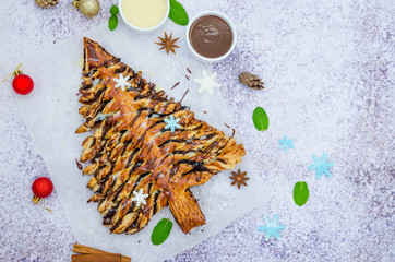Christmas tree pastry with cinnamon and cocoa filling served with chocolate sauces on a stone background.  Dessert for Christmas and New Year.