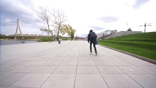 Fitness skating with backpack on wide promenade in slow motion