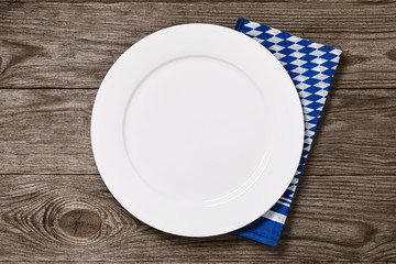 Empty white plate with bavarian napkin on a wooden table, top view. Food background